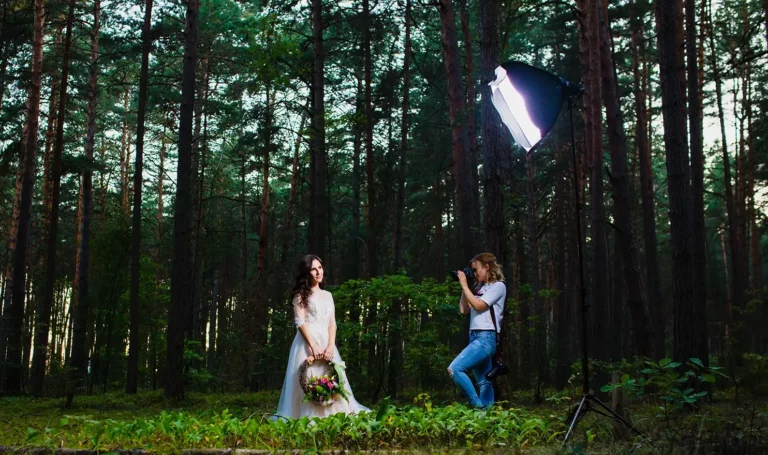 Photographer photographing model wearing a white dress in a dark green forest.