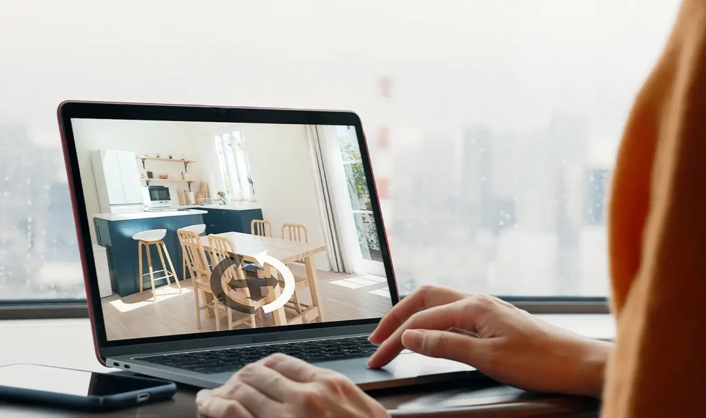 A close-up of a user on a laptop utilizing a 360-degree tool to view the kitchen of a house or apartment.