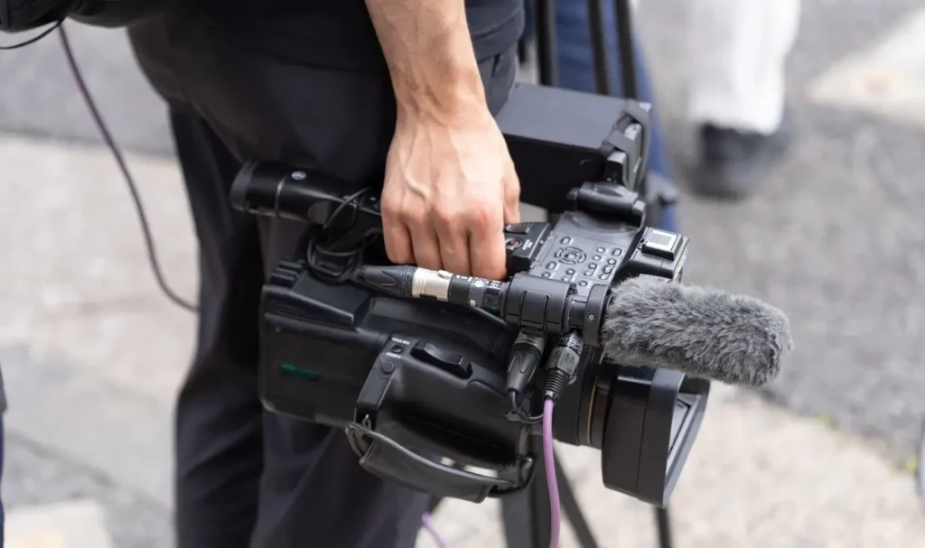 Close-up of a videographer in black clothes, holding their camera with an attached mic at their side.