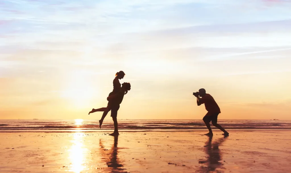 Photographer taking a photo of a couple on a beach at sunset.