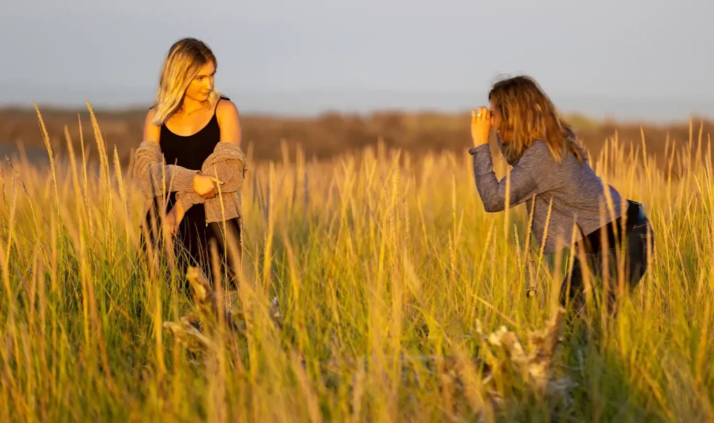 Brunette photographer taking a photo of a blonde model in a field of tall grass.