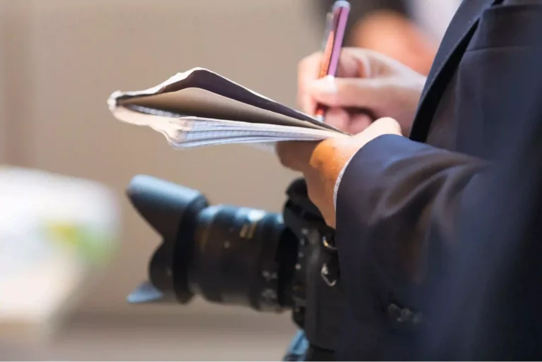 Photojournalist with a camera, pen, and notepad taking notes for an important news story.