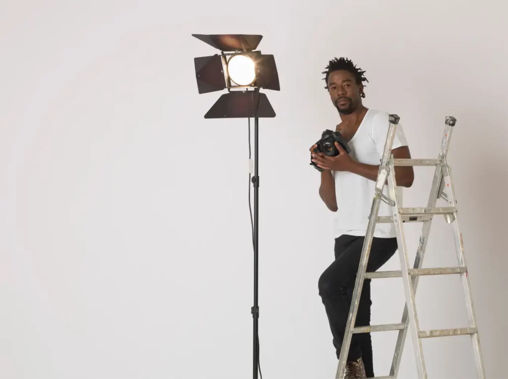 A photographer in his studio holding a camera leaning against a ladder