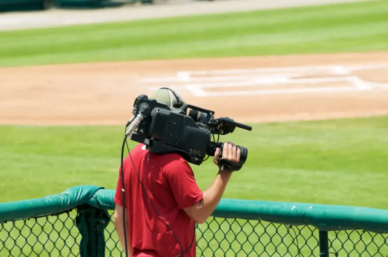 A camera man waiting to get footage at a local baseball field.